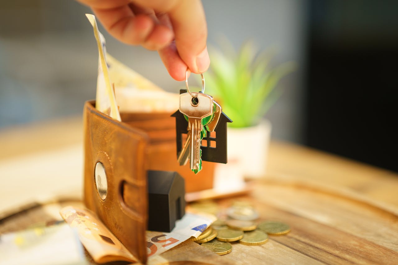 Close-up of hand holding a house key with a wallet and coins, symbolizing real estate investment.